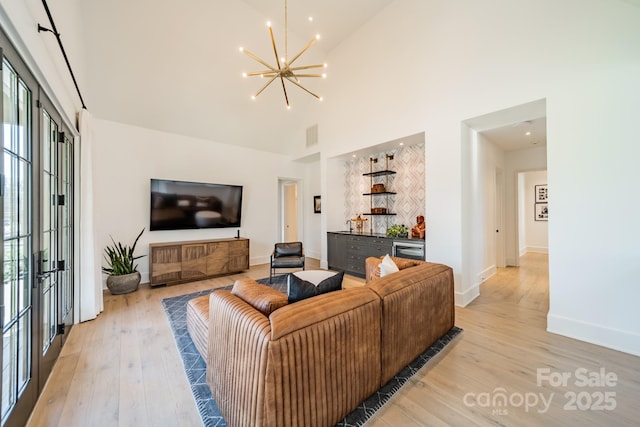 living room with a high ceiling, a chandelier, and light hardwood / wood-style floors