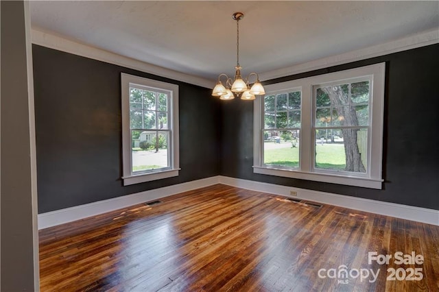 unfurnished dining area with hardwood / wood-style flooring, crown molding, and a notable chandelier