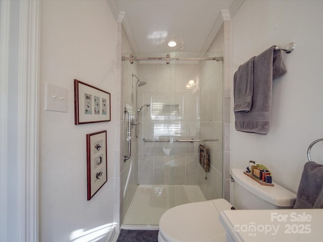 bathroom with toilet, a shower with door, and crown molding