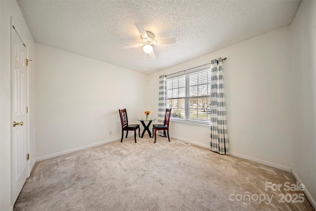 living area with a textured ceiling, light colored carpet, and ceiling fan