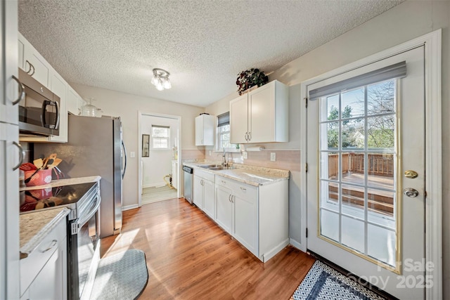 kitchen featuring white cabinets, sink, light hardwood / wood-style flooring, a textured ceiling, and stainless steel appliances