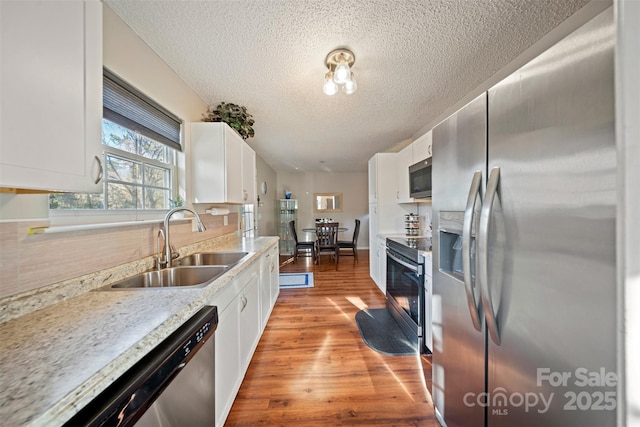 kitchen with appliances with stainless steel finishes, light hardwood / wood-style flooring, white cabinetry, and sink