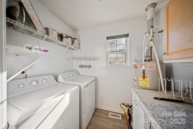 washroom featuring cabinets, gas water heater, light hardwood / wood-style flooring, independent washer and dryer, and a textured ceiling