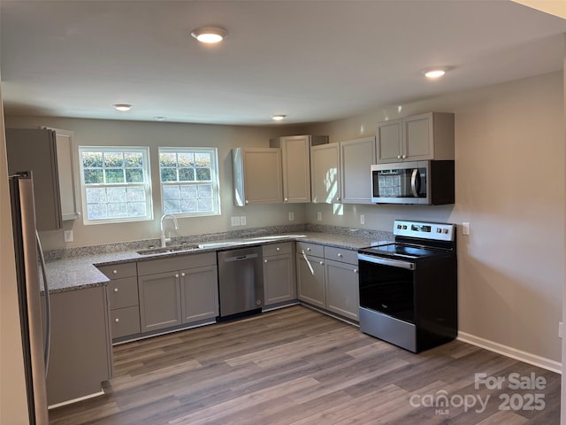 kitchen featuring sink, light stone counters, gray cabinets, appliances with stainless steel finishes, and hardwood / wood-style flooring