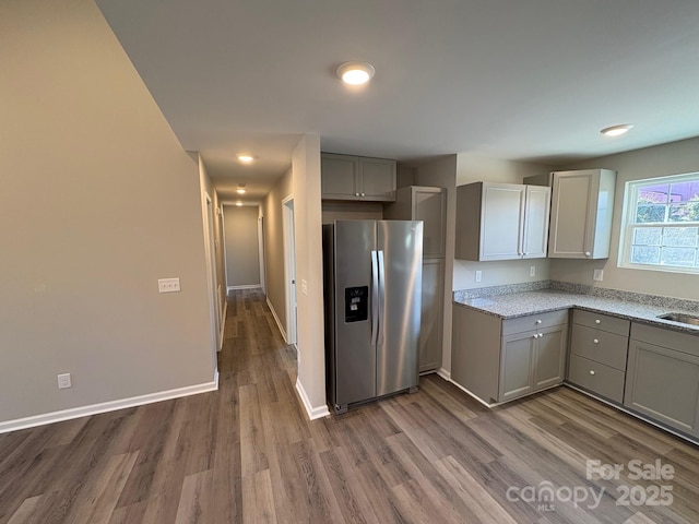 kitchen with gray cabinetry, light stone countertops, wood-type flooring, and stainless steel refrigerator with ice dispenser