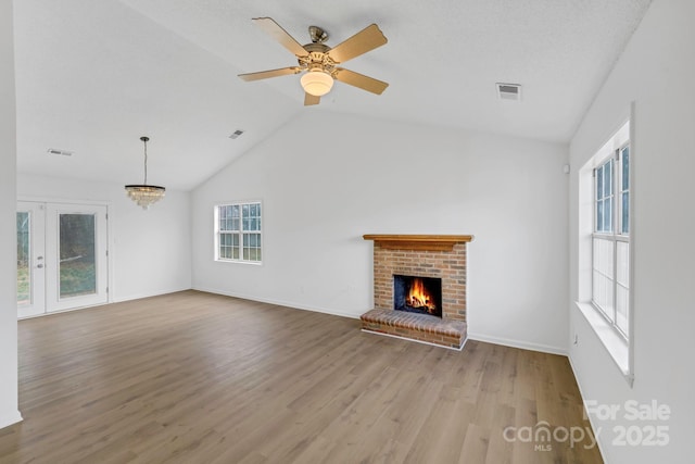 unfurnished living room featuring ceiling fan with notable chandelier, a textured ceiling, light hardwood / wood-style floors, vaulted ceiling, and a brick fireplace