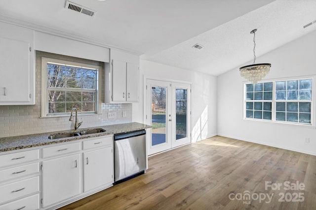 kitchen featuring vaulted ceiling, pendant lighting, stainless steel dishwasher, sink, and white cabinets