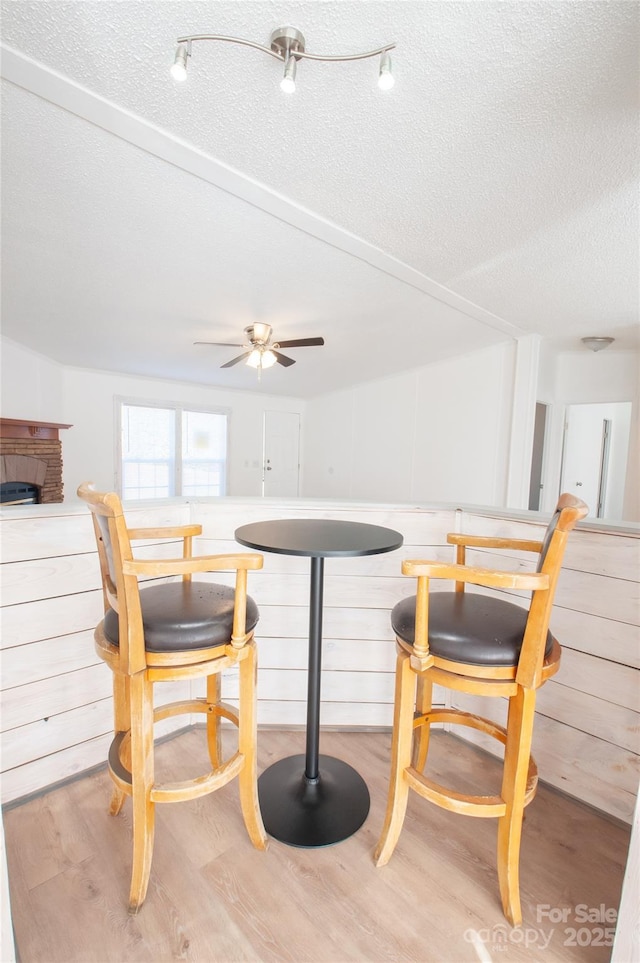 dining room with a textured ceiling, ceiling fan, a fireplace, and light hardwood / wood-style flooring