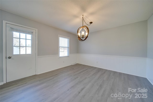 spare room with a textured ceiling, light wood-type flooring, and an inviting chandelier