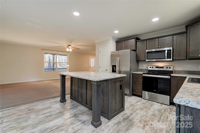 kitchen featuring dark brown cabinetry, ceiling fan, appliances with stainless steel finishes, a kitchen island, and ornamental molding