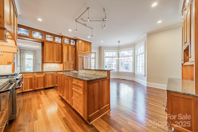 kitchen with high end range, light stone countertops, backsplash, light hardwood / wood-style floors, and a kitchen island