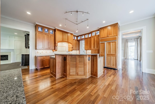 kitchen featuring tasteful backsplash, a kitchen island with sink, crown molding, and light stone counters