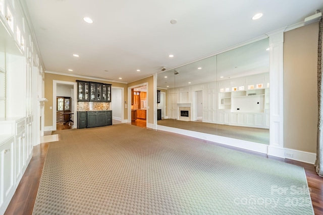 unfurnished living room with indoor bar, dark wood-type flooring, and crown molding