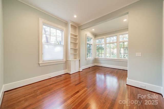 empty room featuring built in shelves, crown molding, plenty of natural light, and hardwood / wood-style flooring