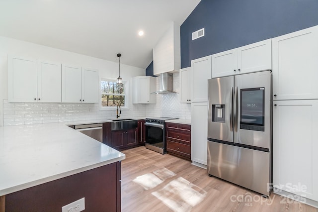 kitchen featuring white cabinets, wall chimney exhaust hood, appliances with stainless steel finishes, light wood-style floors, and a sink