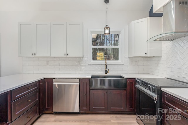 kitchen featuring range with electric cooktop, light wood-style flooring, light countertops, wall chimney range hood, and stainless steel dishwasher