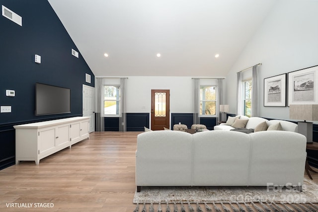 living area with visible vents, wainscoting, light wood-type flooring, high vaulted ceiling, and recessed lighting