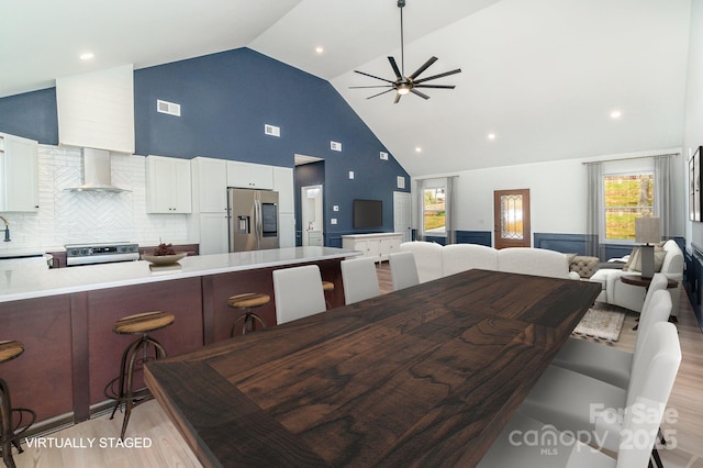 dining room with ceiling fan, high vaulted ceiling, light wood-style flooring, and visible vents