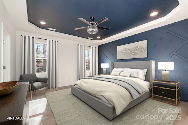 bedroom with a raised ceiling, wood finished floors, and recessed lighting