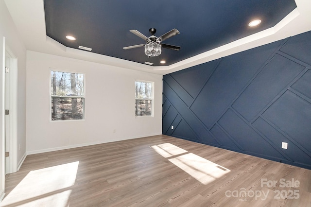 empty room featuring a tray ceiling, wood finished floors, visible vents, and recessed lighting