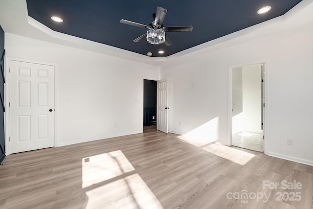 unfurnished bedroom featuring light wood-type flooring, a tray ceiling, baseboards, and recessed lighting