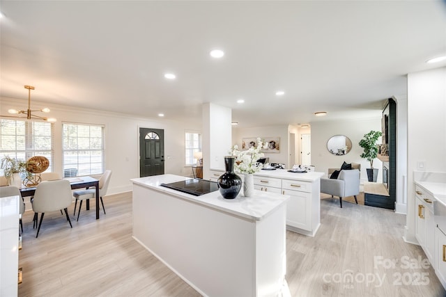 kitchen featuring a kitchen island, light hardwood / wood-style floors, decorative light fixtures, black electric cooktop, and white cabinets