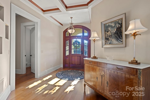 foyer entrance with beamed ceiling, light wood-type flooring, ornamental molding, and coffered ceiling