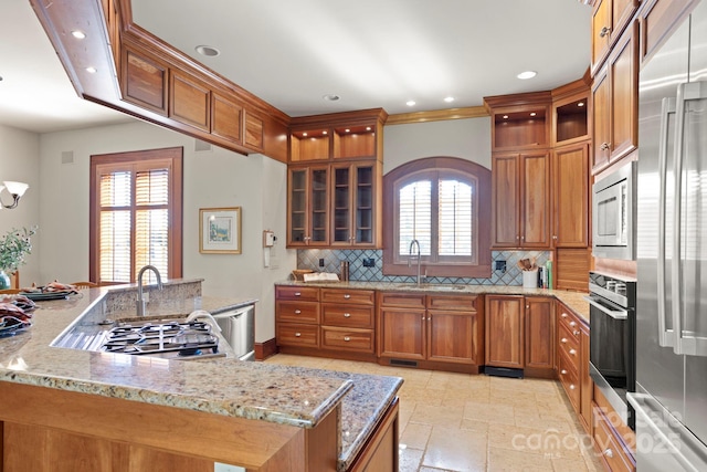 kitchen with sink, tasteful backsplash, light stone counters, kitchen peninsula, and stainless steel appliances