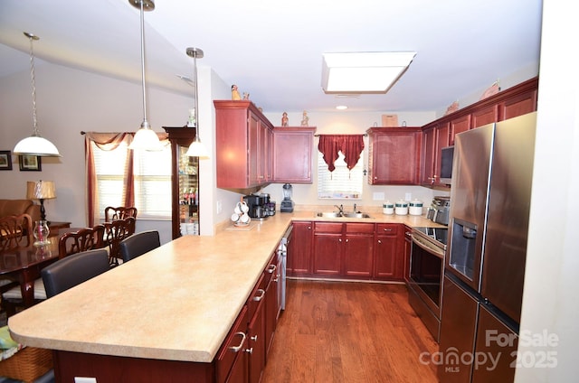 kitchen featuring sink, dark wood-type flooring, a kitchen breakfast bar, pendant lighting, and appliances with stainless steel finishes