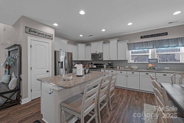 kitchen with light stone countertops, a center island with sink, a breakfast bar, white cabinets, and appliances with stainless steel finishes