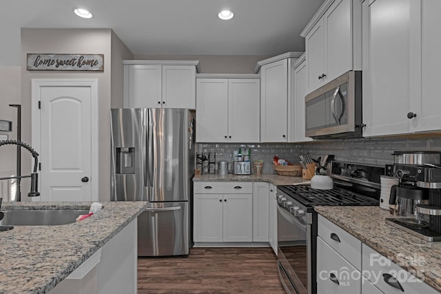 kitchen with stainless steel appliances, white cabinetry, sink, and light stone countertops