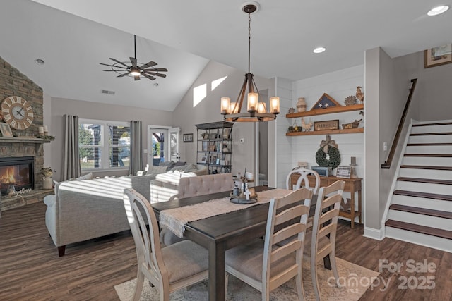 dining area featuring dark hardwood / wood-style flooring, lofted ceiling, ceiling fan with notable chandelier, and a fireplace