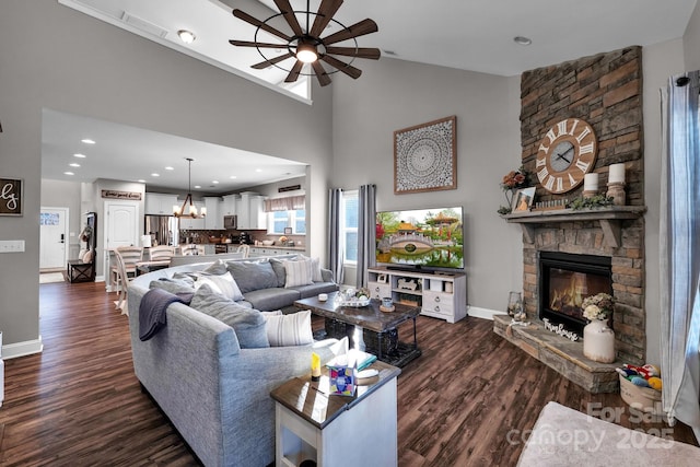 living room featuring ceiling fan with notable chandelier, dark hardwood / wood-style flooring, a towering ceiling, and a stone fireplace