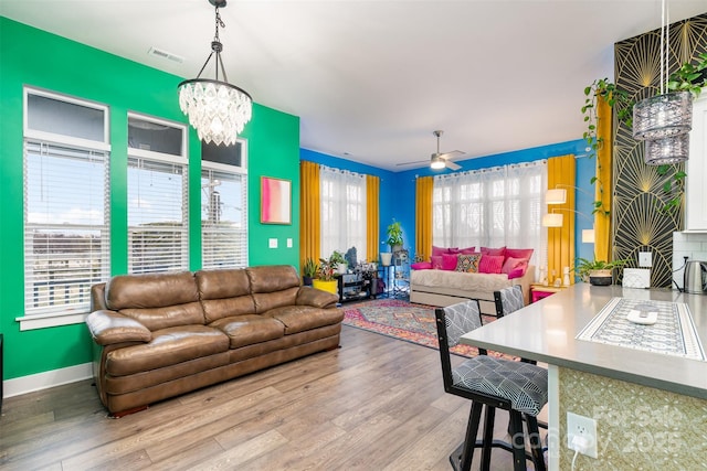 living room featuring ceiling fan with notable chandelier, a healthy amount of sunlight, and light hardwood / wood-style flooring