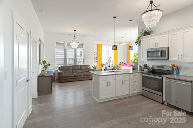 kitchen featuring stainless steel appliances, a peninsula, white cabinetry, open floor plan, and hanging light fixtures