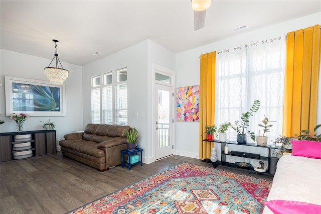 living area featuring baseboards, visible vents, dark wood-style flooring, and ceiling fan with notable chandelier