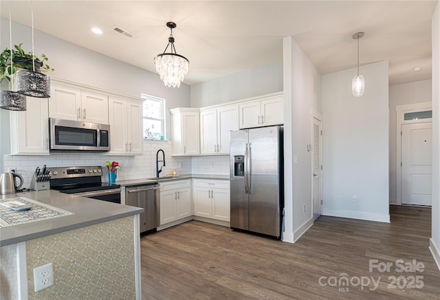 kitchen featuring stainless steel appliances, white cabinets, decorative light fixtures, and a sink