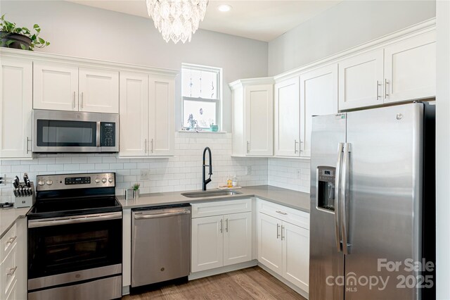 kitchen with stainless steel appliances, light countertops, decorative backsplash, white cabinetry, and a sink