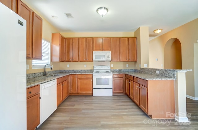 kitchen with white appliances, sink, light hardwood / wood-style floors, light stone counters, and kitchen peninsula