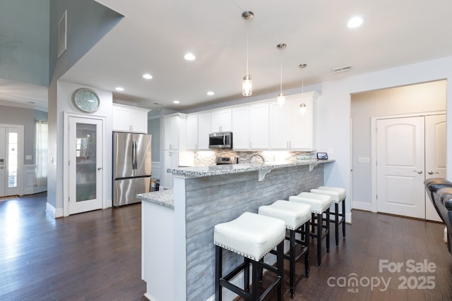 kitchen with appliances with stainless steel finishes, a kitchen breakfast bar, light stone counters, decorative light fixtures, and white cabinets