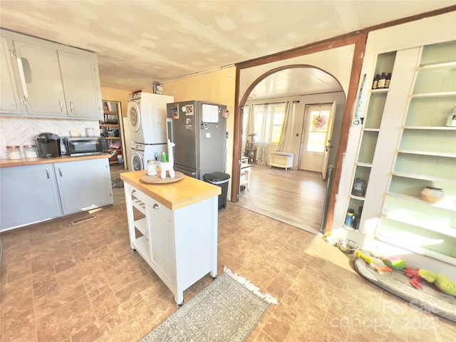 kitchen featuring stainless steel refrigerator, white cabinets, backsplash, wooden counters, and stacked washer / drying machine