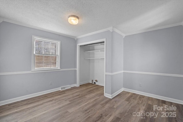 unfurnished bedroom featuring a closet, wood-type flooring, a textured ceiling, and ornamental molding