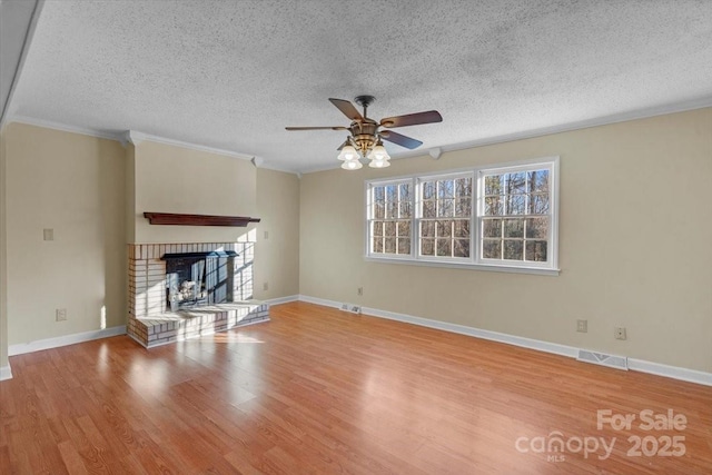 unfurnished living room with ceiling fan, a brick fireplace, crown molding, light hardwood / wood-style floors, and a textured ceiling