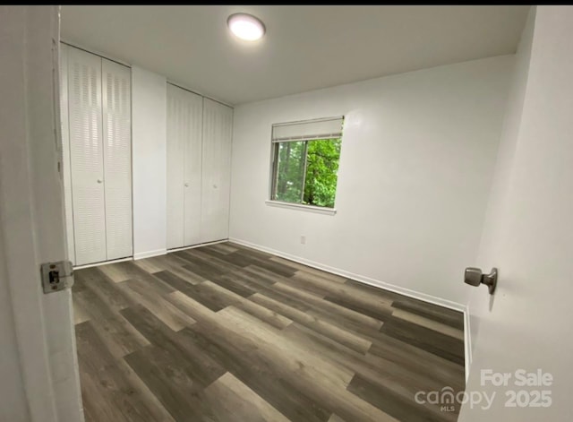 unfurnished bedroom featuring multiple closets and dark hardwood / wood-style floors