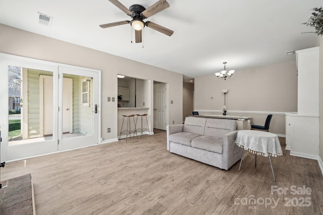 living room with visible vents, ceiling fan with notable chandelier, baseboards, and wood finished floors