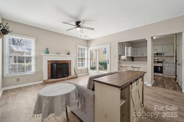 living area featuring ceiling fan, baseboards, a brick fireplace, and wood finished floors