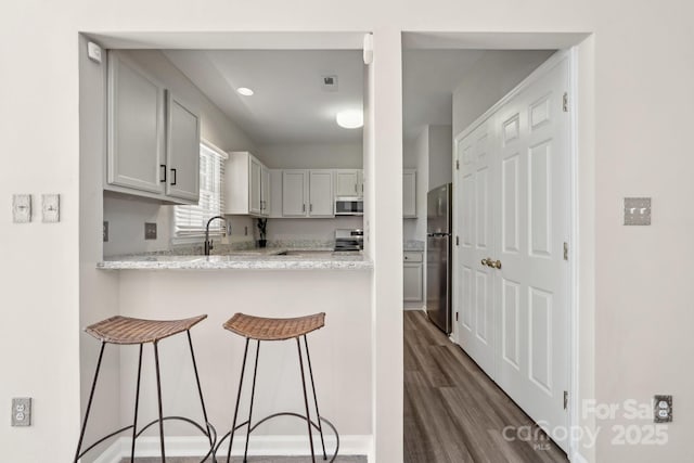 kitchen with dark wood-style floors, a peninsula, a sink, stainless steel appliances, and a kitchen bar