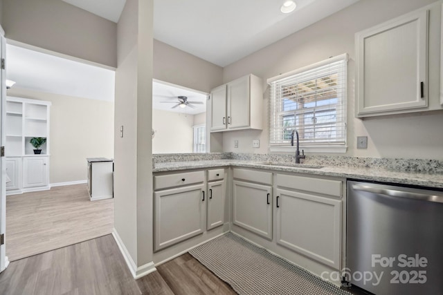 kitchen featuring a sink, stainless steel dishwasher, wood finished floors, baseboards, and ceiling fan