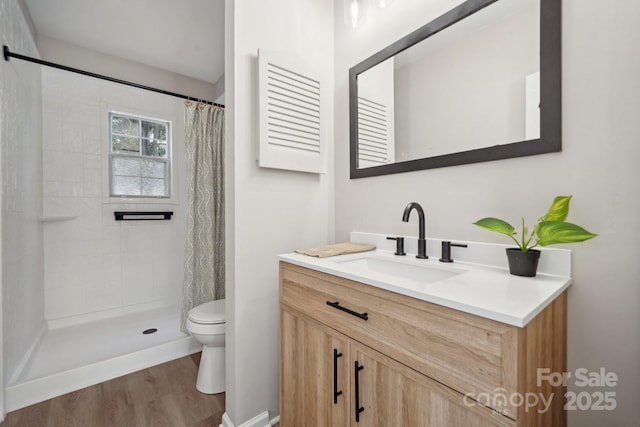 bathroom featuring vanity, toilet, wood finished floors, and tiled shower