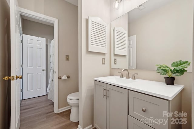 bathroom with toilet, vanity, baseboards, and wood finished floors